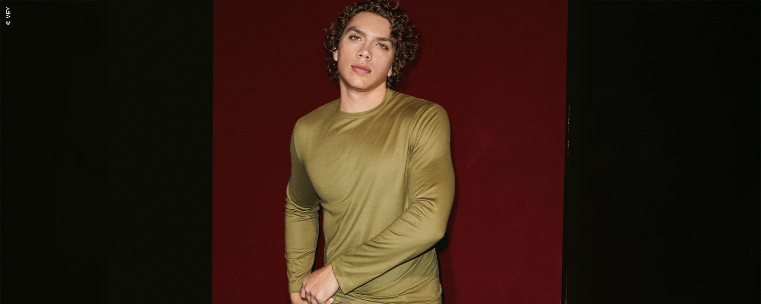 Mann trägt ein olivgrünes Longsleeve vor rotem Hintergrund.