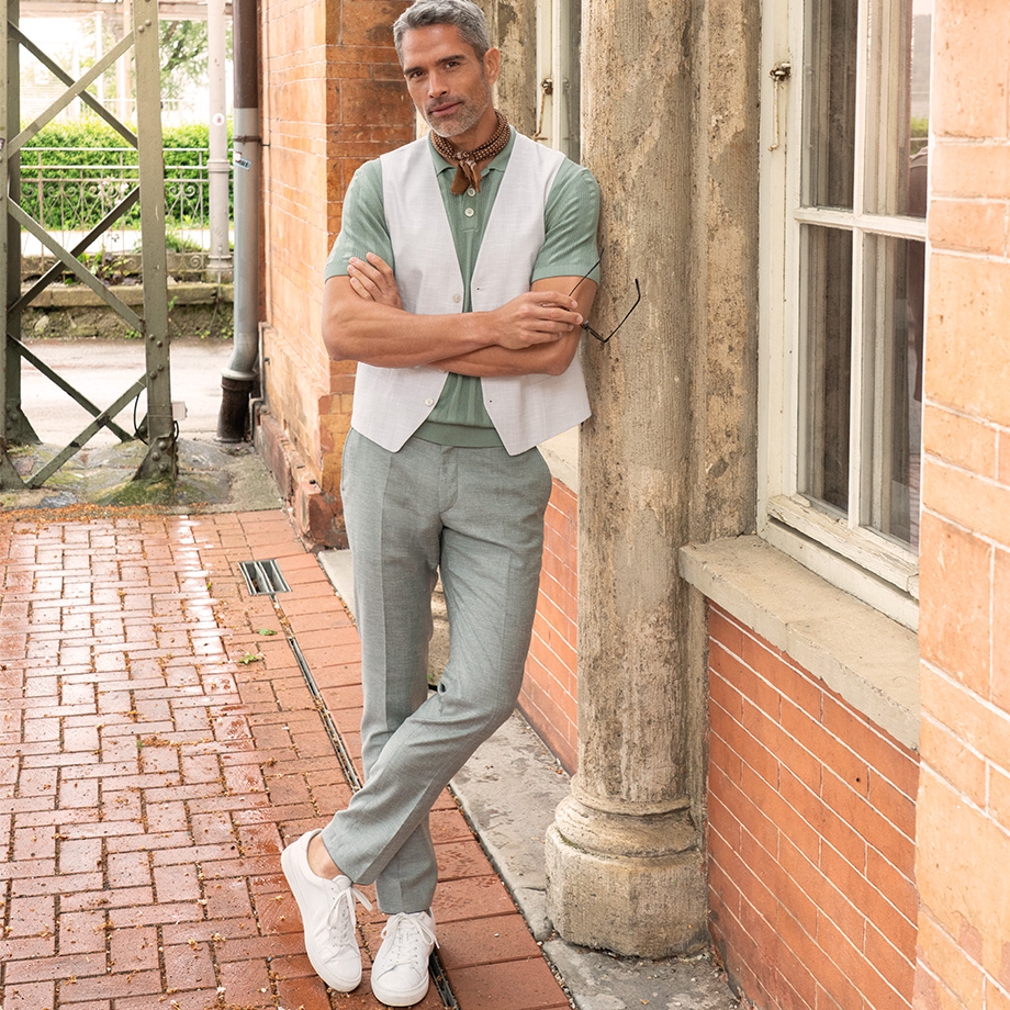 Elegante graue Leinenhose mit mintgrünem Poloshirt und weißer Weste, lässig mit Sneakers getragen