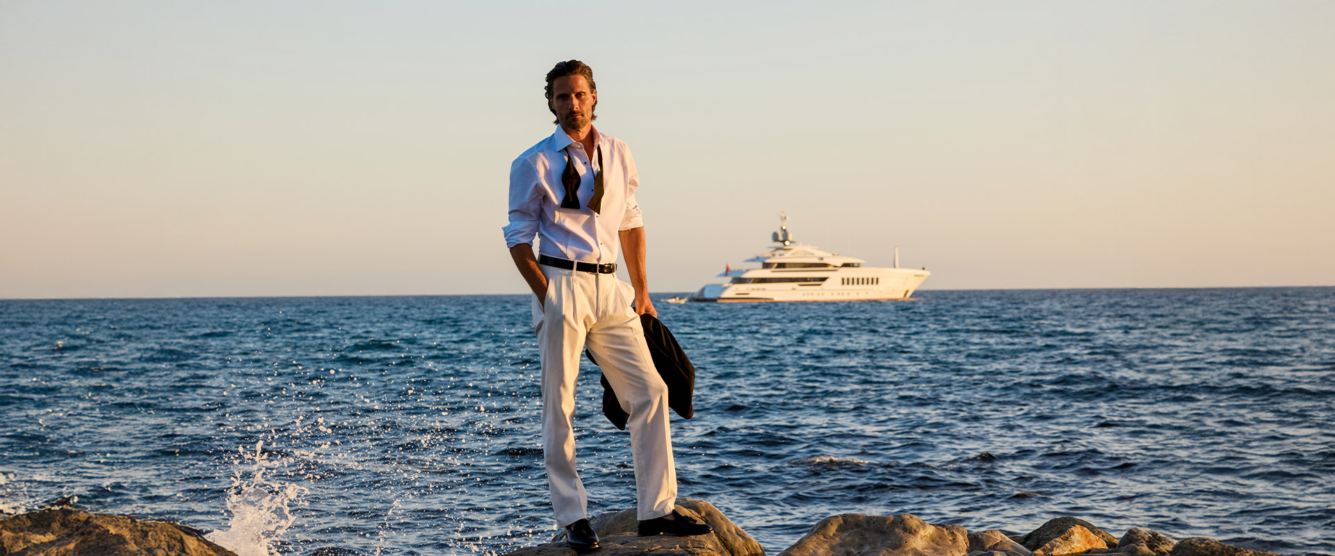 Mann im weißen Business-Hemd und heller Hose an der Küste, mit Krawatte locker gebunden