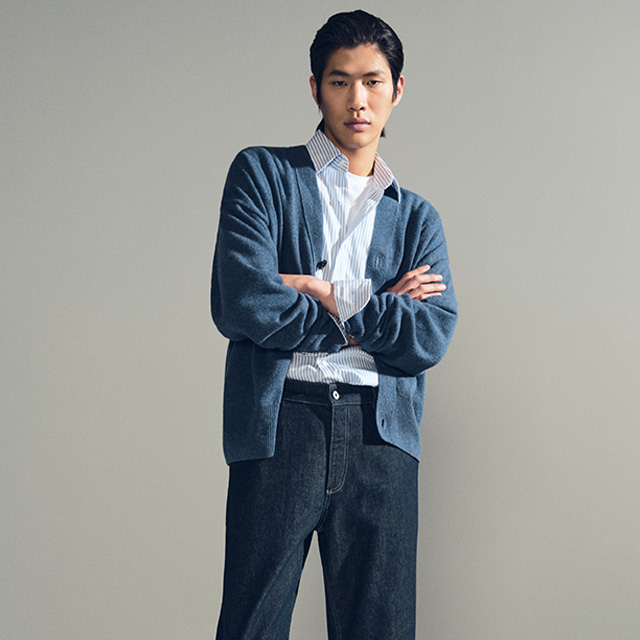 Mann in blauem Cardigan und gestreiftem Hemd, getragen mit dunkler Jeans, lässig elegant präsentiert