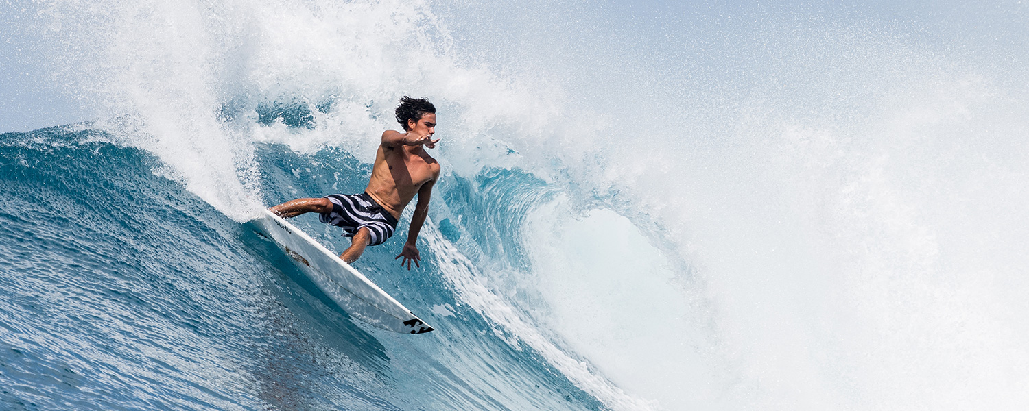 Surfer in schwarz-weißer Badehose auf großer Welle, dynamisch dargestellt