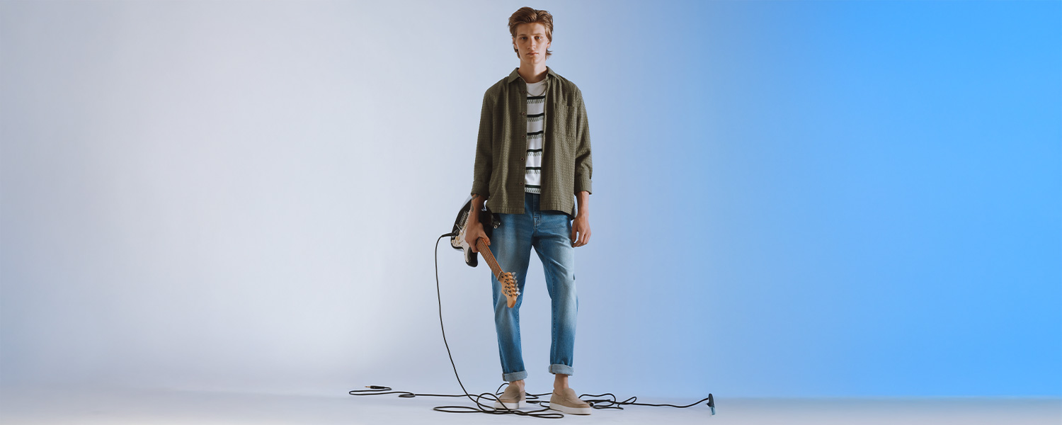 Grünes Freizeit-Hemd über weißem Streifen-T-Shirt, blaue Jeans, lässig mit E-Gitarre