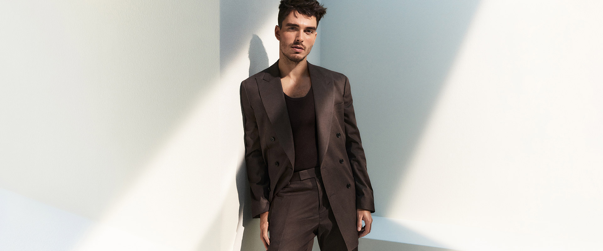 Mann in braunem Anzug mit passendem T-Shirt, lässig angelehnt an Wand