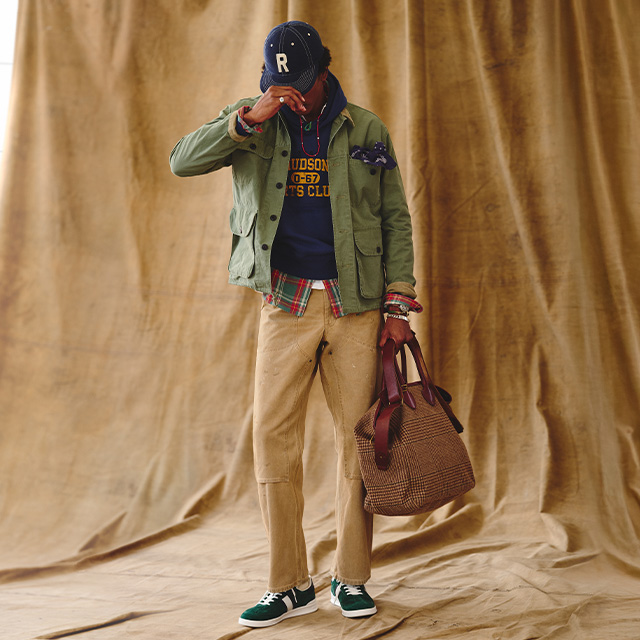 Casual-Look mit olivgrüner Jacke, kariertem Hemd, Sweatshirt und beigefarbener Hose, kombiniert mit Tasche und Cap