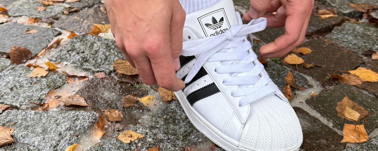 Weißer Sneaker mit schwarzen Streifen, aus Leder, auf Kopfsteinpflaster mit Herbstblättern, von Hand geschnürt