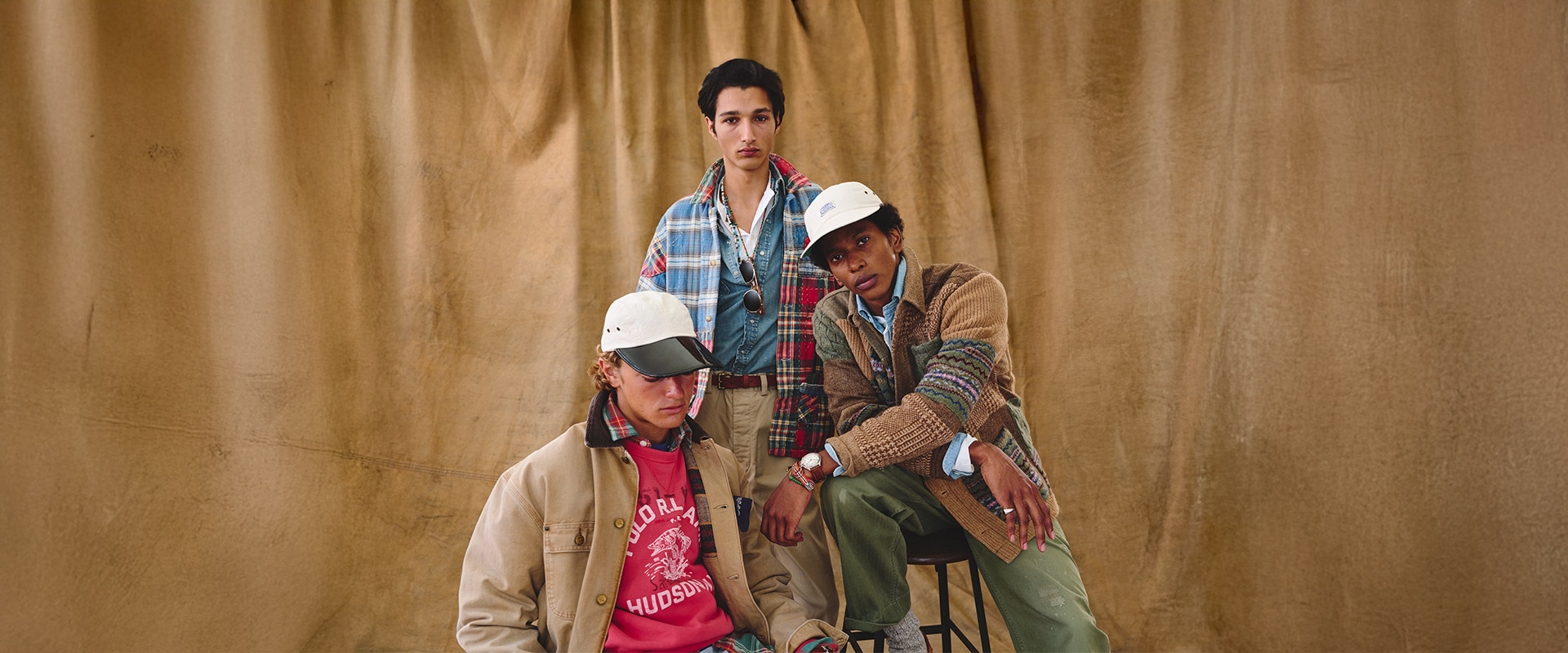 Drei Männer in karierten Hemden und Strickjacken, lässig präsentiert vor braunem Hintergrund