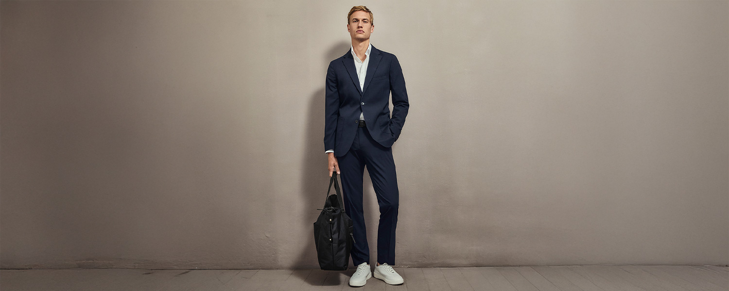 Mann in dunkelblauem Anzug mit weißem Hemd und weißen Sneakers, lässig mit Tasche