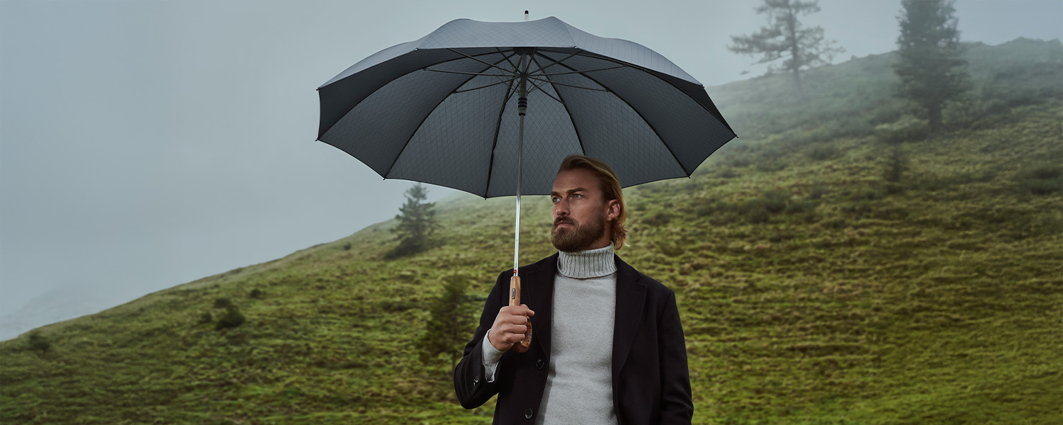 Mann in grauem Rollkragen-Strickpullover mit schwarzem Mantel und Regenschirm im Freien