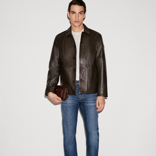 Mann in brauner Lederjacke mit Jeans und weißem T-Shirt, lässig präsentiert