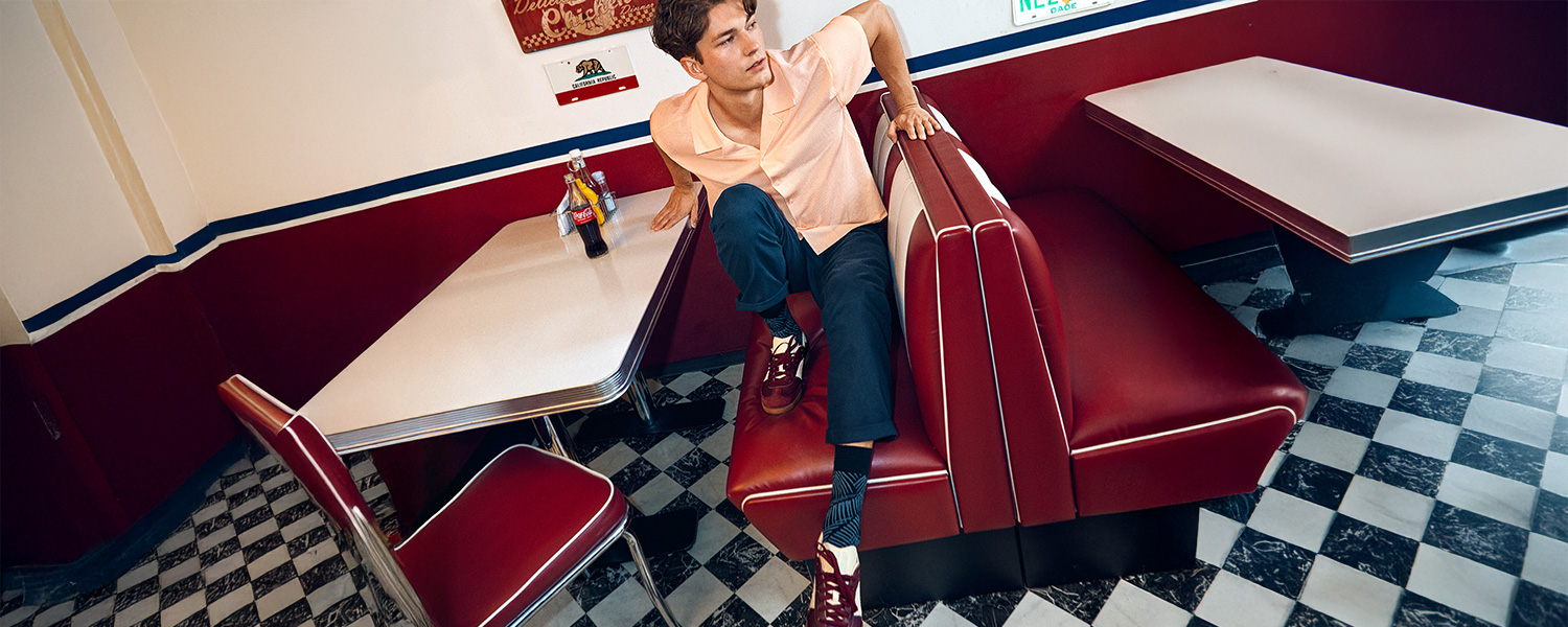 Herr in apricotfarbenem Kurzarmhemd und dunkler Hose, lässig in Retro-Diner sitzend