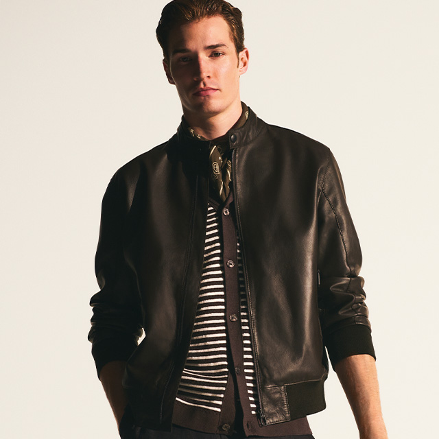 Mann in schwarzer Lederjacke, gestreiftes Shirt darunter, stehend