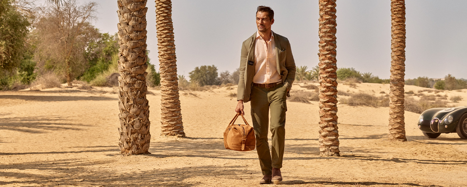 Mann in olivgrünem Anzug und rosa Hemd mit Reisetasche, casual im Freien