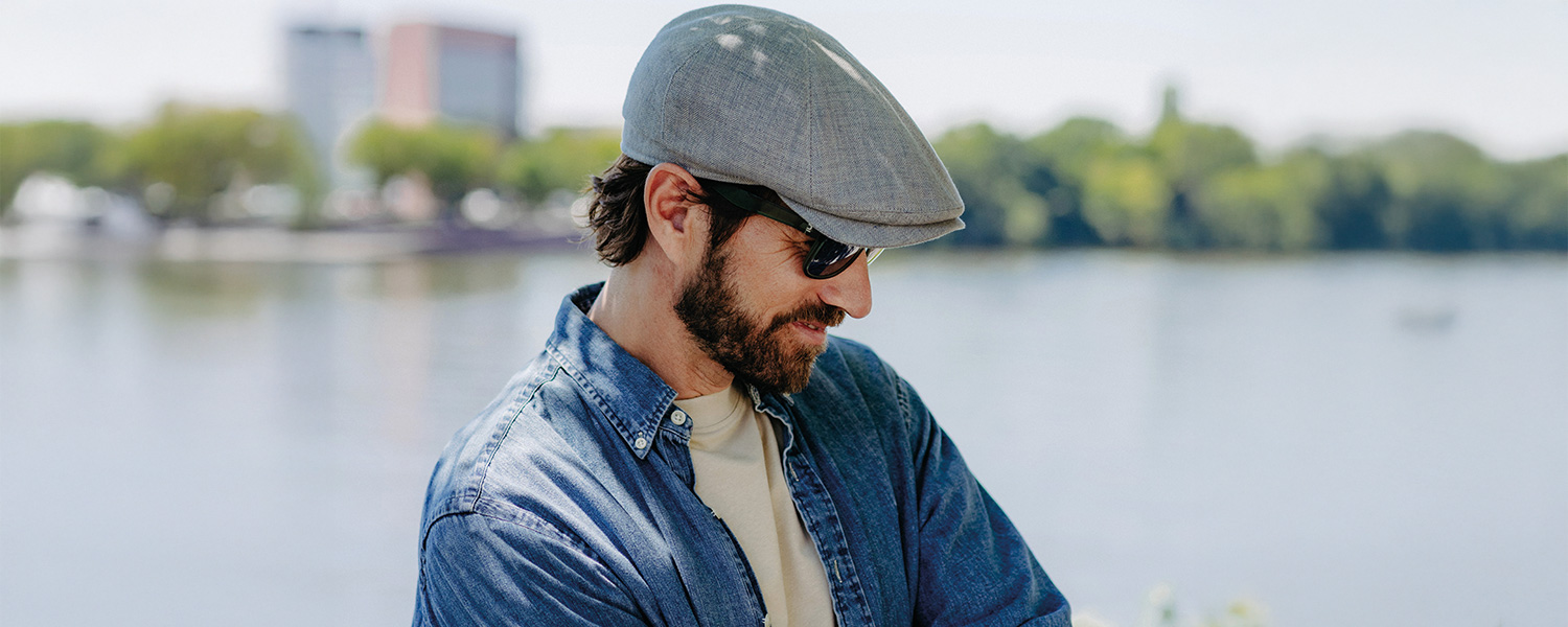 Mann mit grauer Schiebermütze und Jeanshemd am Seeufer