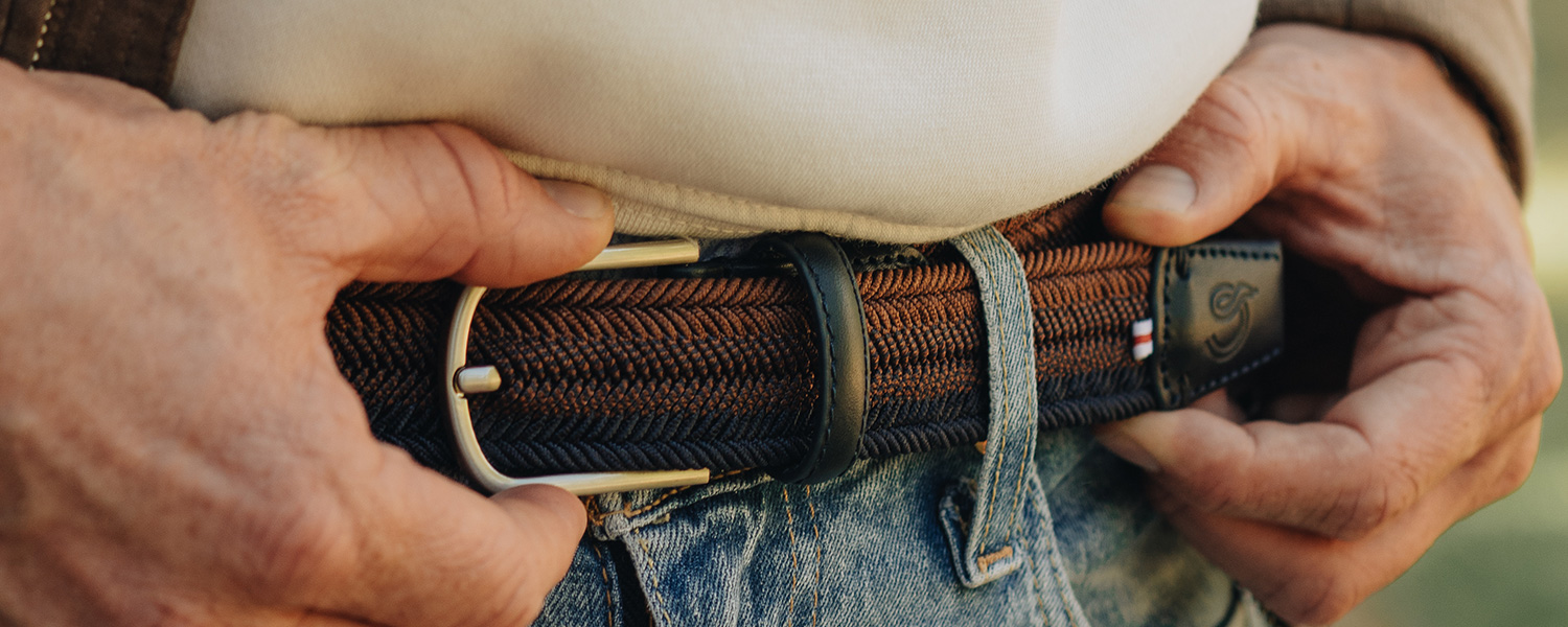 Geflochtener Gürtel in Braun-Schwarz an Jeans getragen, Detail von Metallschnalle und Lederakzent