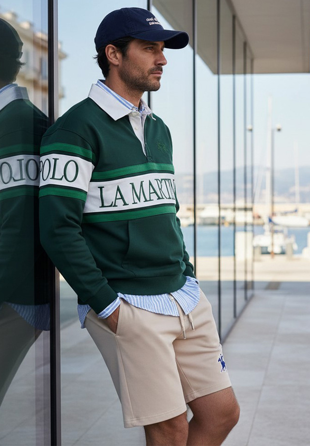 Mann in grünem Rugbyshirt mit Schriftzug und beigen Shorts, lässig gestylt