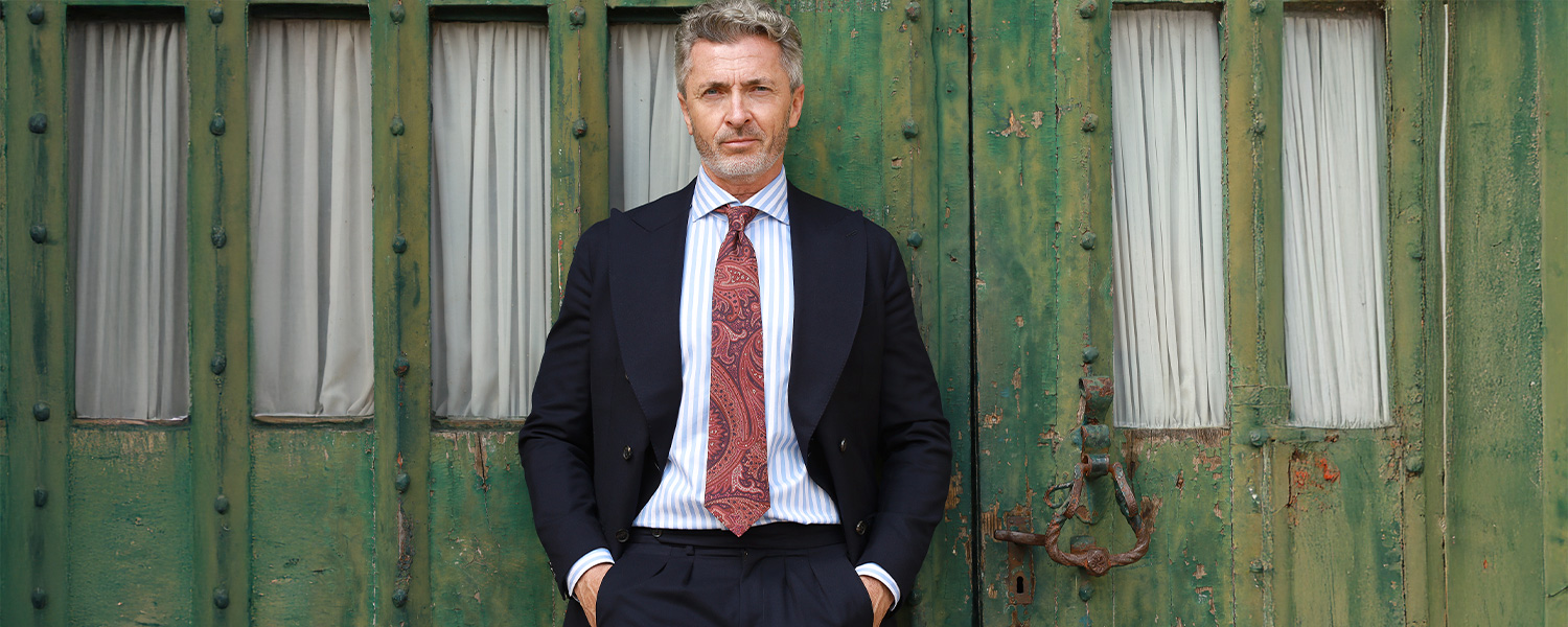 Mann in dunkelblauem Anzug mit gestreiftem Hemd und Paisley-Krawatte vor grüner Tür