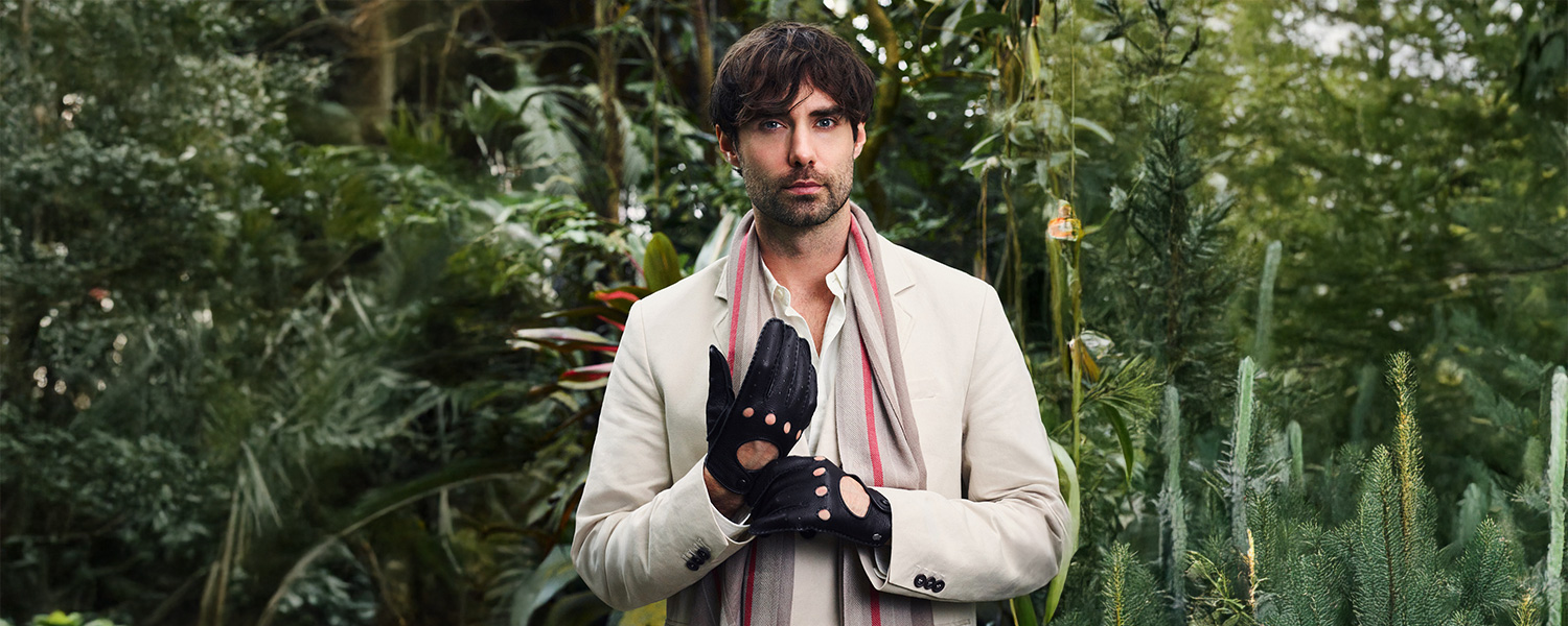 Mann mit cremefarbenem Sakko und gestreiftem Schal im Grünen