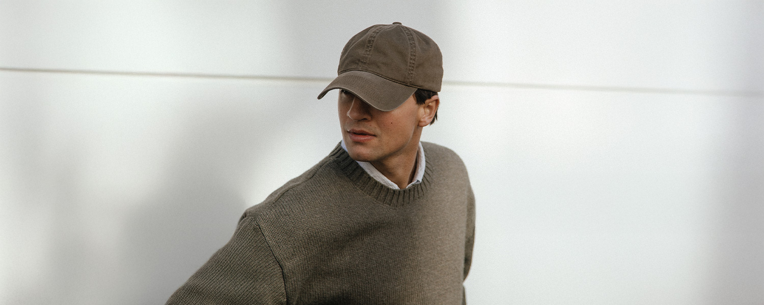 Mann in olivfarbenem Strickpullover und brauner Baseballkappe vor weißem Hintergrund