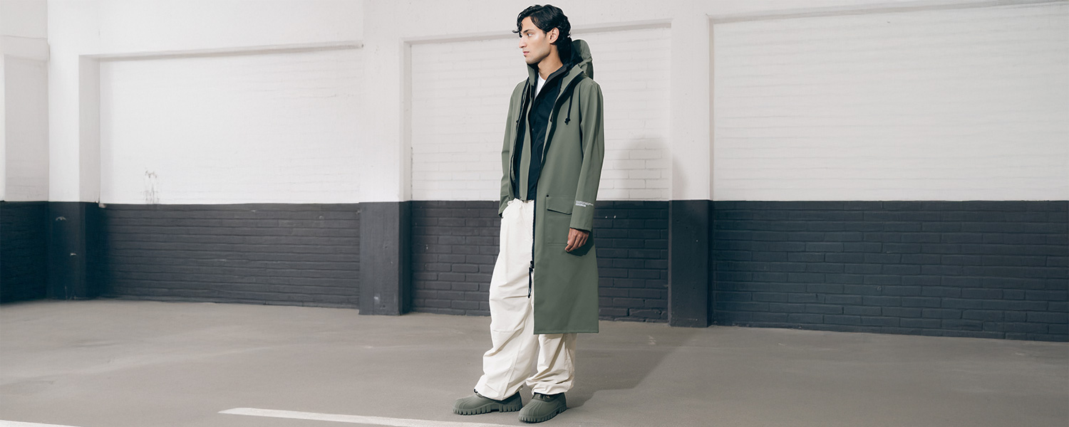 Mann in olivfarbenem Mantel mit Kapuze, weiße Hose, lässiger Look in urbaner Umgebung