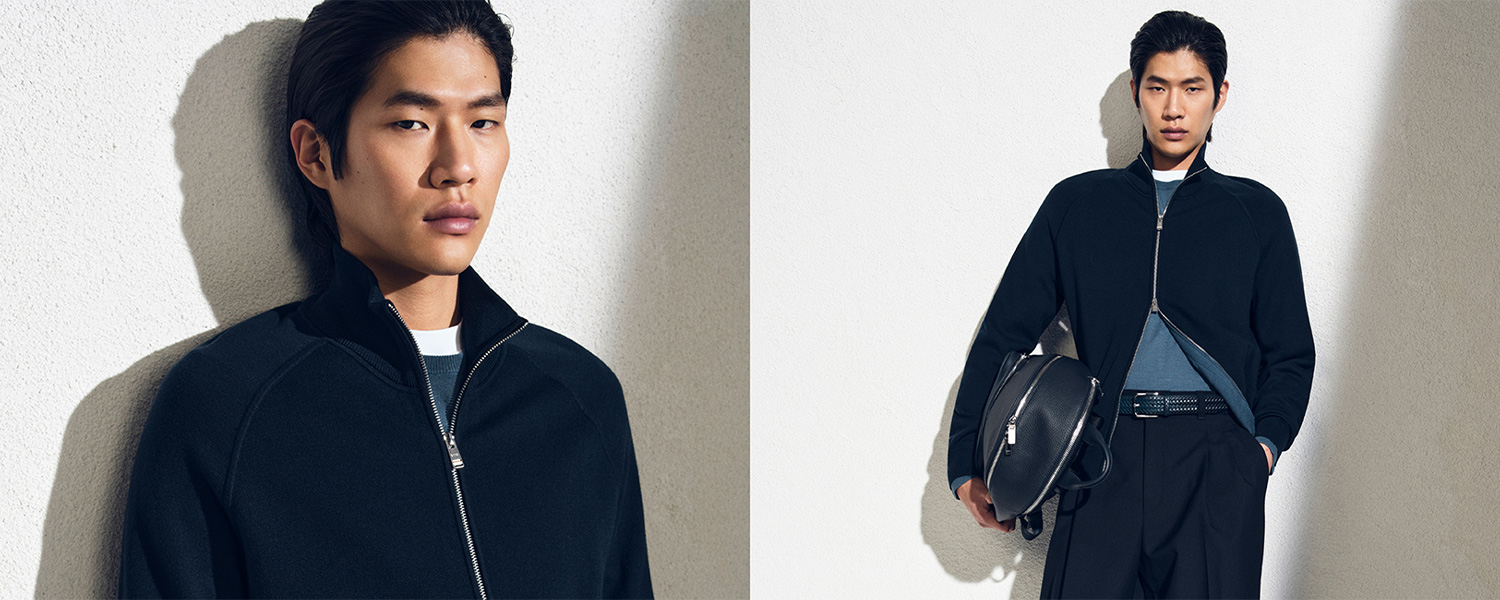 Mann in schwarzer Strickjacke mit Reißverschluss, kombiniert mit blauer Hose und Tasche, lässig präsentiert