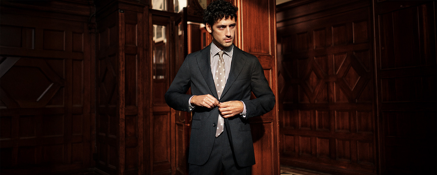 Mann in dunkelgrauem Anzug mit gestreiftem Hemd und gepunkteter Krawatte in holzgetäfeltem Raum