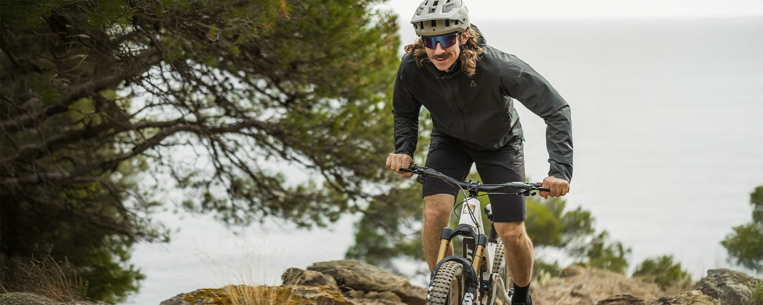Mountainbiker in dunkelgrauer Jacke und Shorts auf Waldweg, Fahrradausrüstung im Gelände