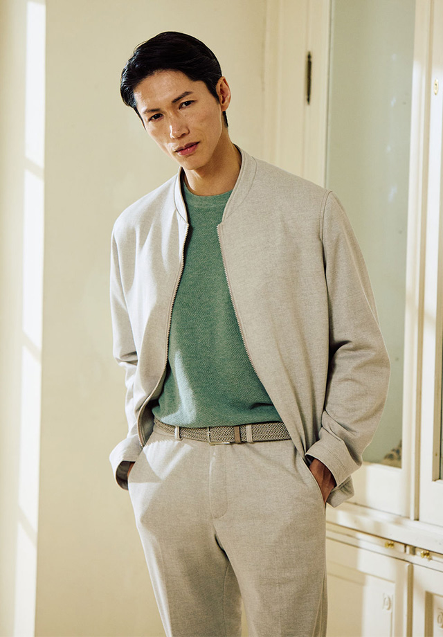 Graumeliertes Freizeit-Outfit mit Jacke und Hose, kombiniert mit grünem Pullover, Mann steht lässig in Innenraum