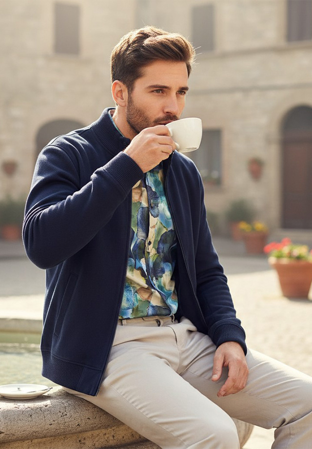 Mann in marineblauer Strickjacke mit floralem Hemd und beigen Chinos, lässig im Freien