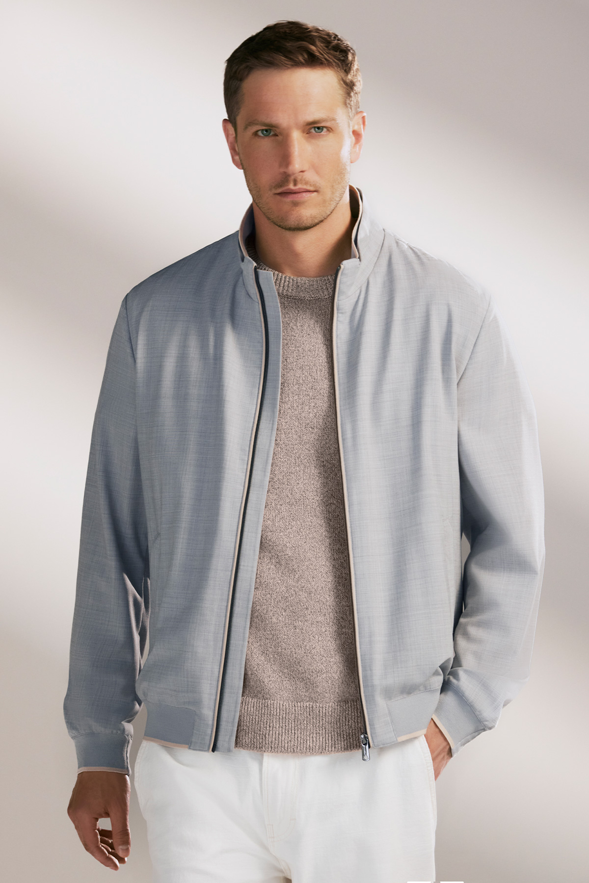 Hellgraue Herrenjacke mit Reißverschluss, kombiniert mit beigefarbenem Strickpullover, lässig getragen