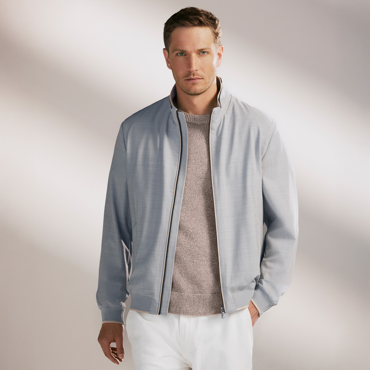 Hellgraue Herrenjacke mit Reißverschluss, kombiniert mit beigefarbenem Strickpullover, lässig getragen