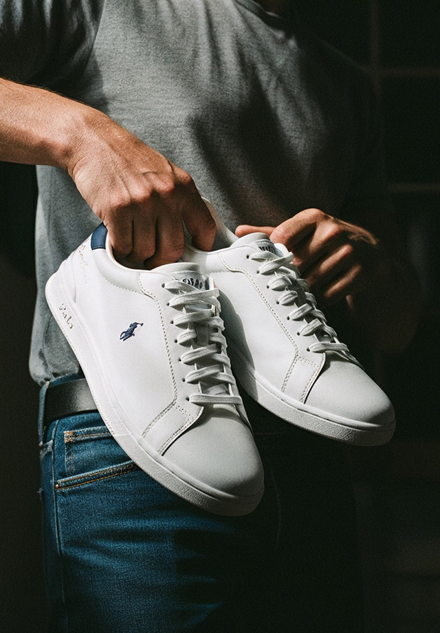 Person hält weiße Leder-Sneaker mit blauem Logo, Freizeitkleidung
