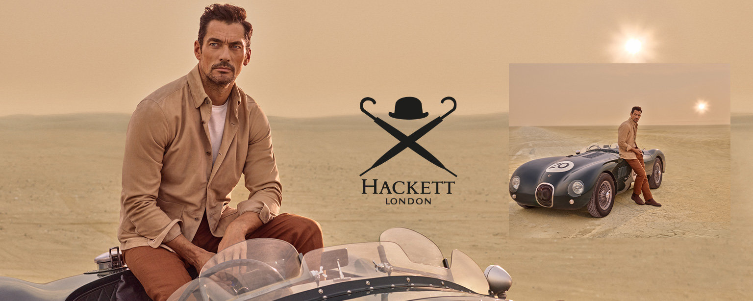 Mann in beigefarbener Jacke und brauner Hose, lässig auf Oldtimer im Wüstenhintergrund sitzend