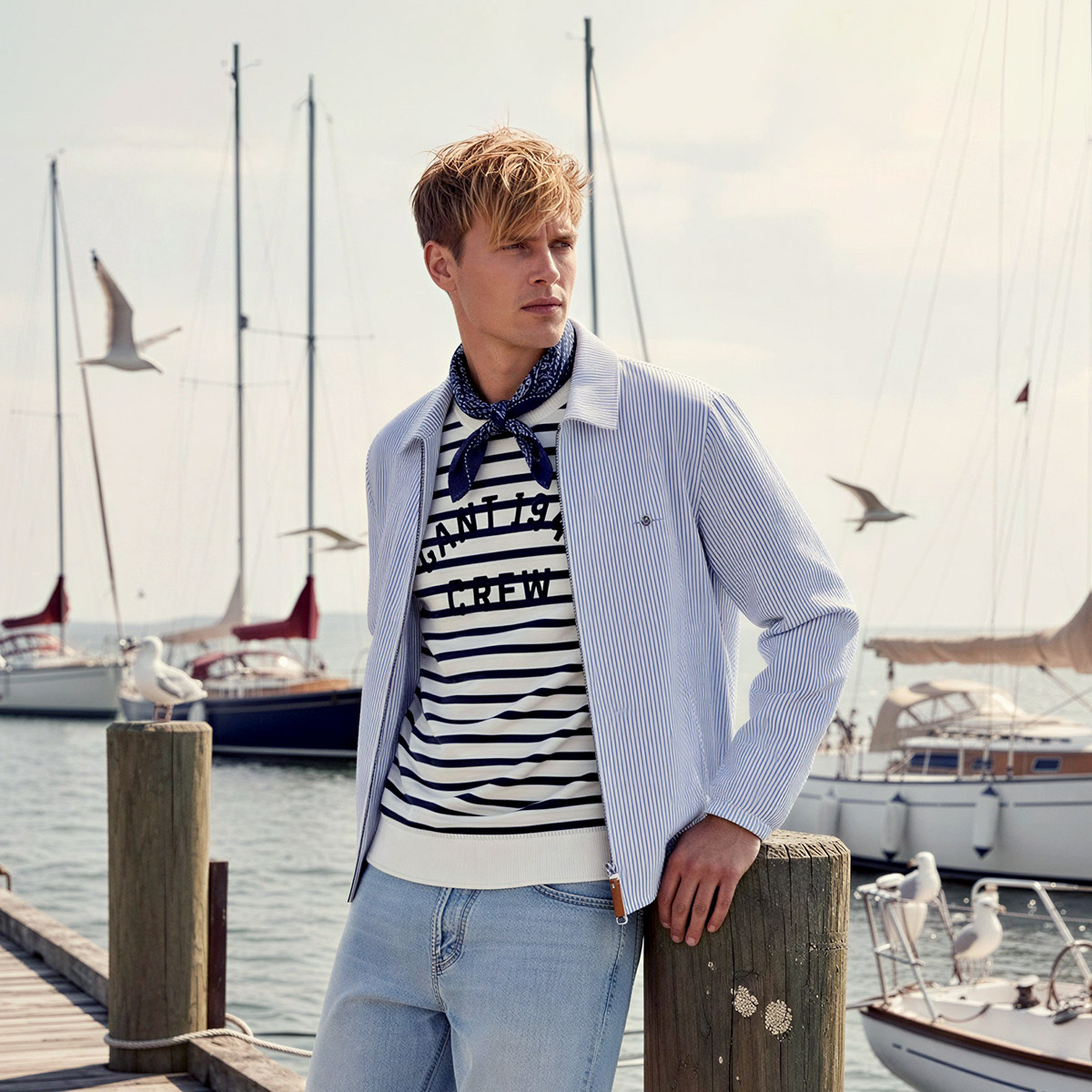 Herr in blau-weiß gestreiftem T-Shirt und hellblauem Hemd am Hafen