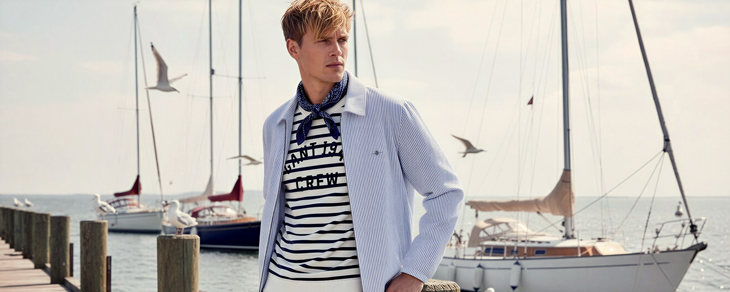 Mann in gestreiftem Marine-T-Shirt mit hellblauer Jacke am Yachthafen