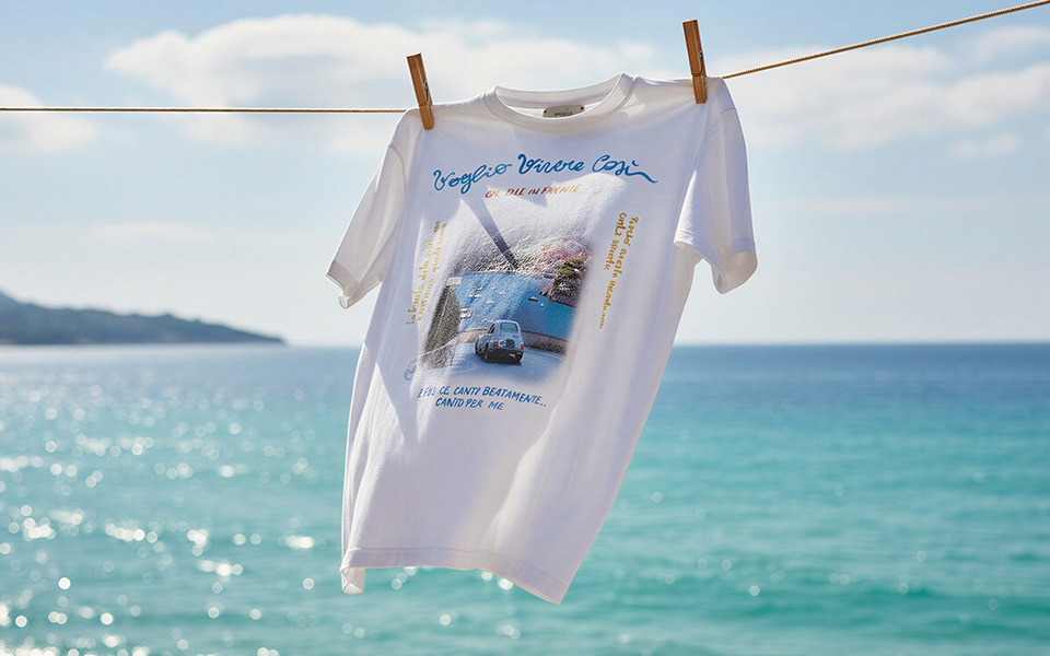 Weißes T-Shirt mit Fotodruck und Schriftzug auf Wäscheleine am Meer