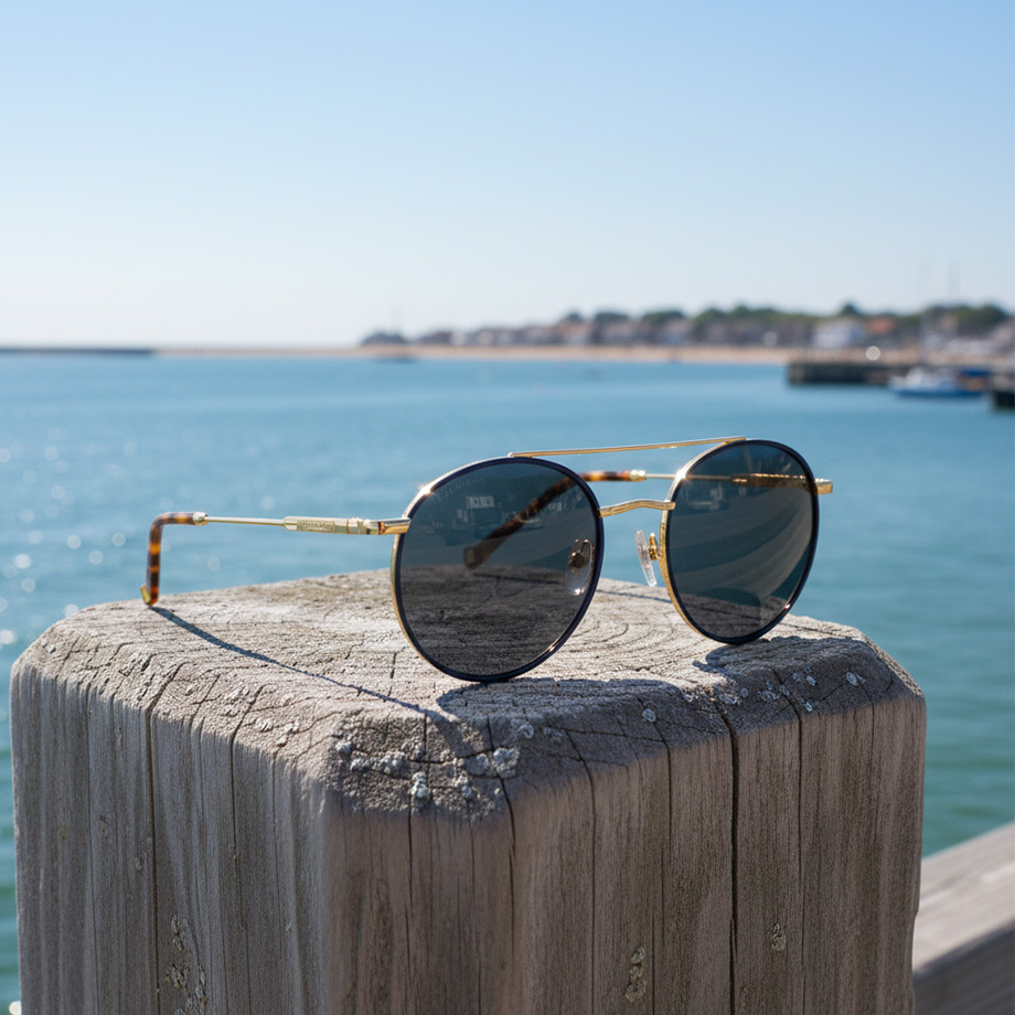 Sonnenbrille mit runden Gläsern und goldfarbenem Gestell auf Holzsteg am Meer platziert
