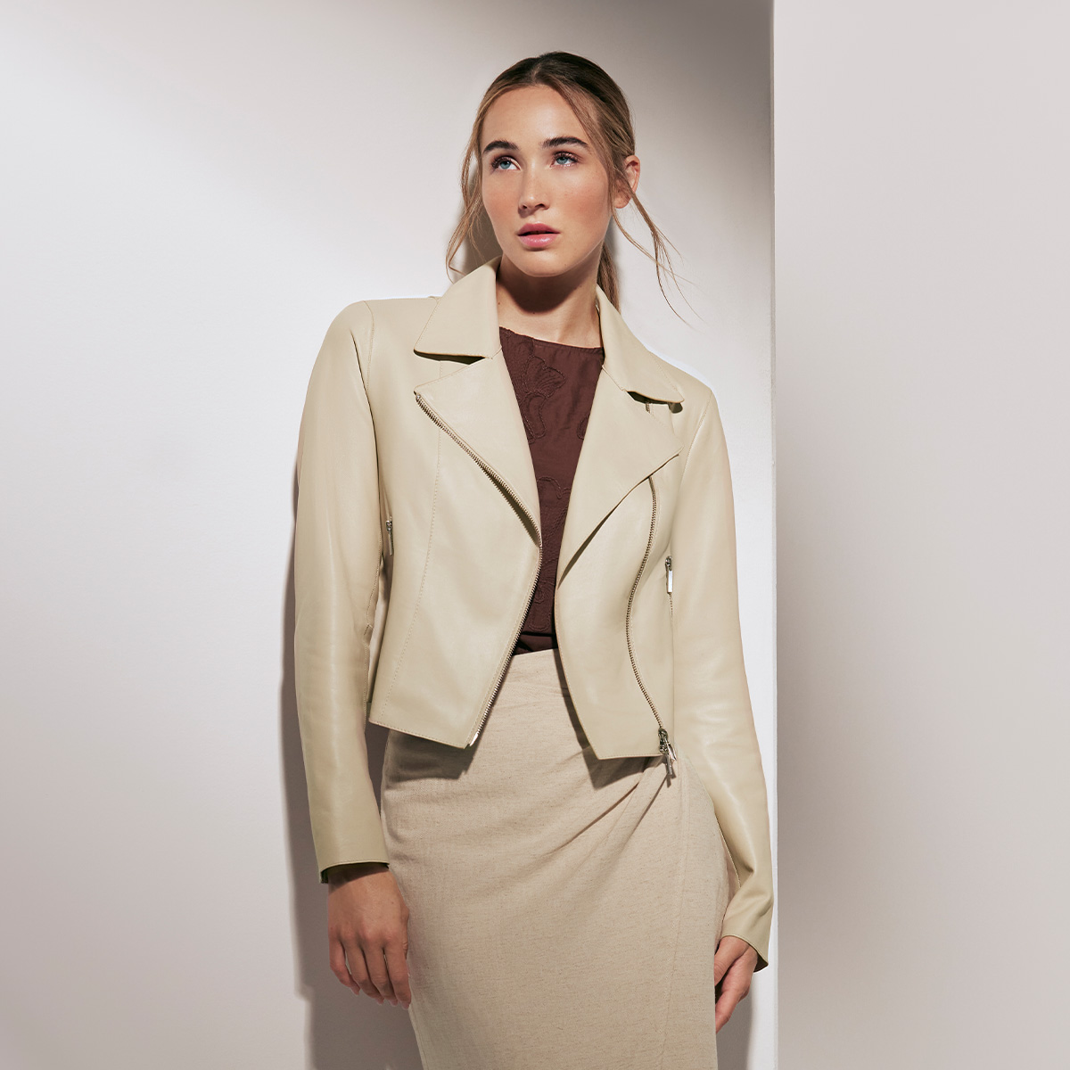 Frau in beige Lederjacke und beigem Rock vor hellem Hintergrund