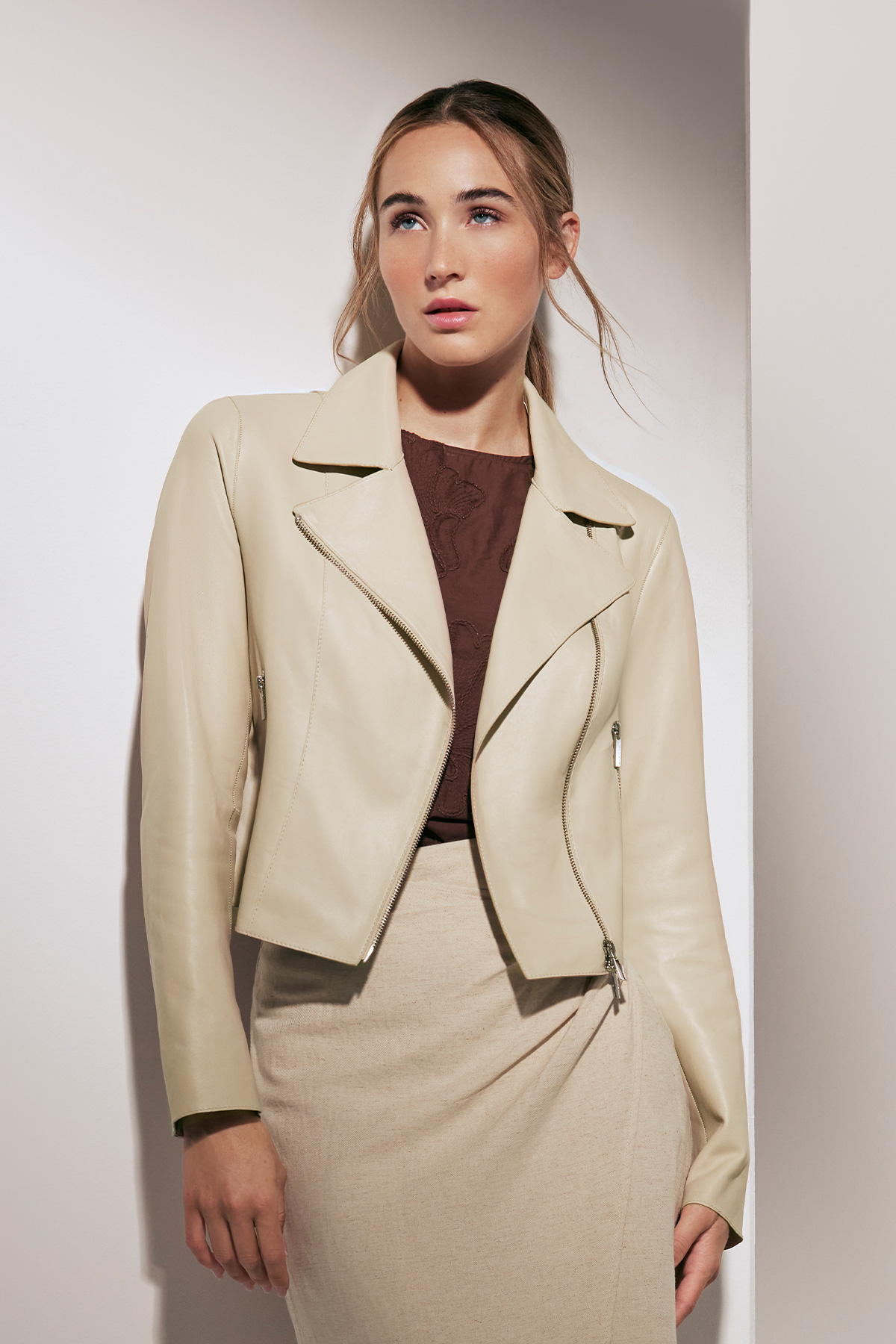 Frau in beige Lederjacke und beigem Rock vor hellem Hintergrund