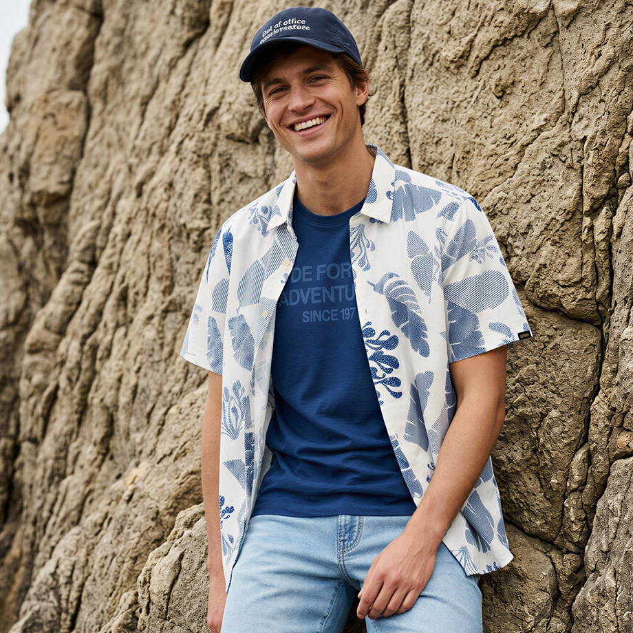 Herr in weißem kurzärmligen Printhemd und blauem T-Shirt vor Felswand