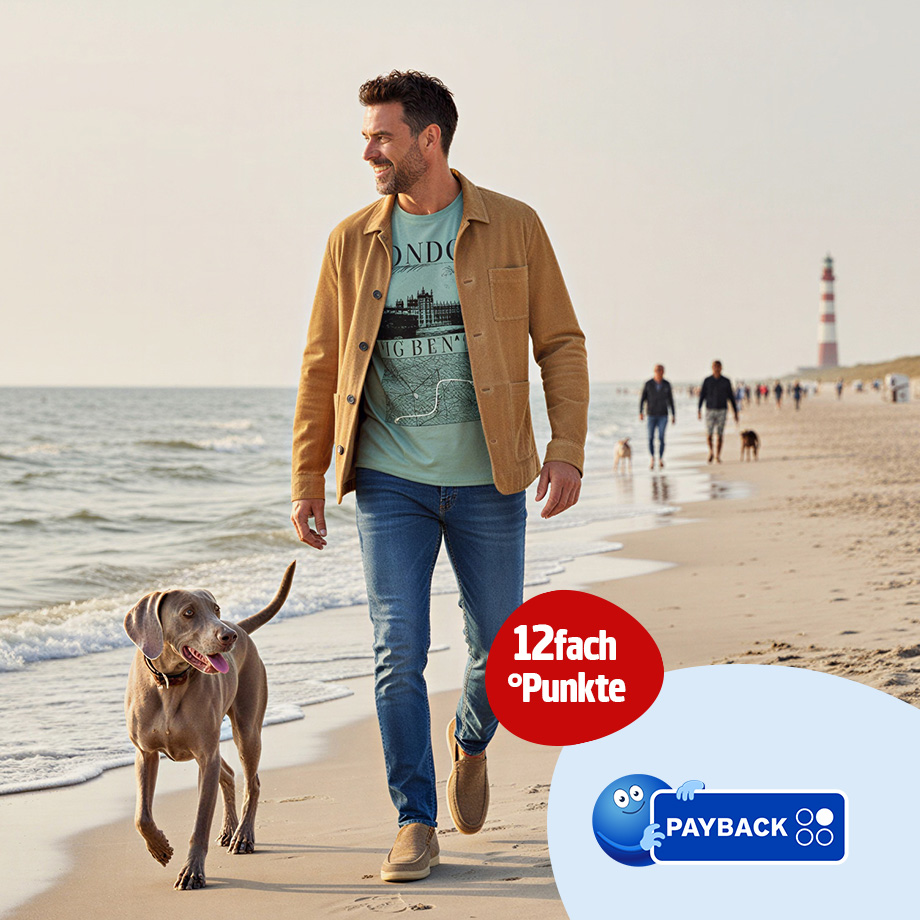 Mann in beiger Jacke und bedrucktem T-Shirt, blaue Jeans, lässig am Strand mit Hund
