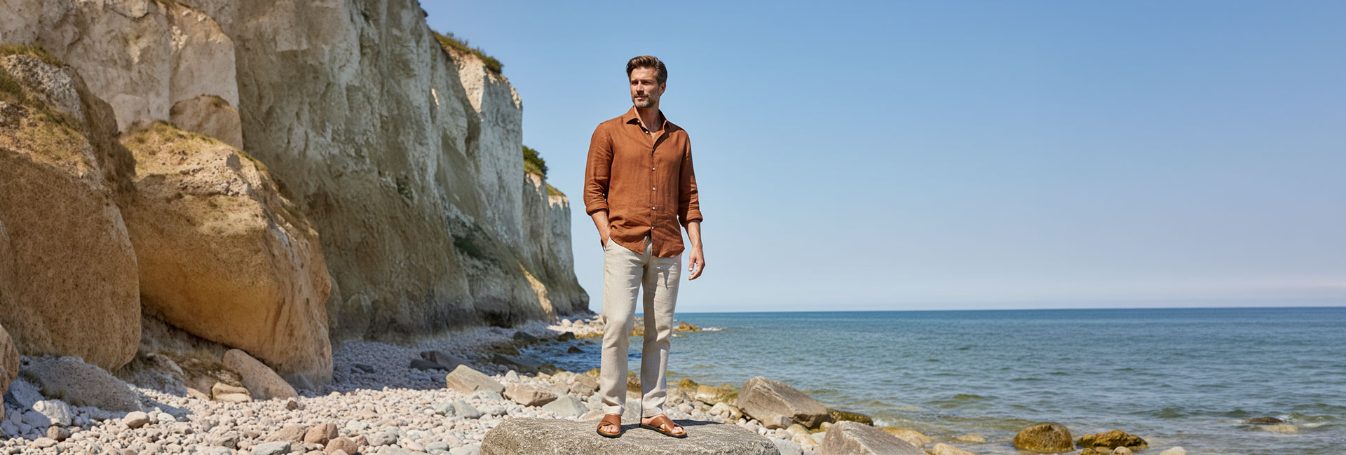 Mann in rostfarbenem Leinenhemd und weißen Leinenhosen am Strand