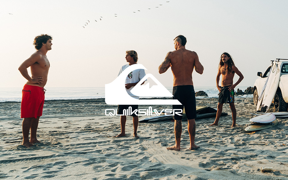 Gruppe von Männern in Badehosen am Strand, Surfboards im Hintergrund