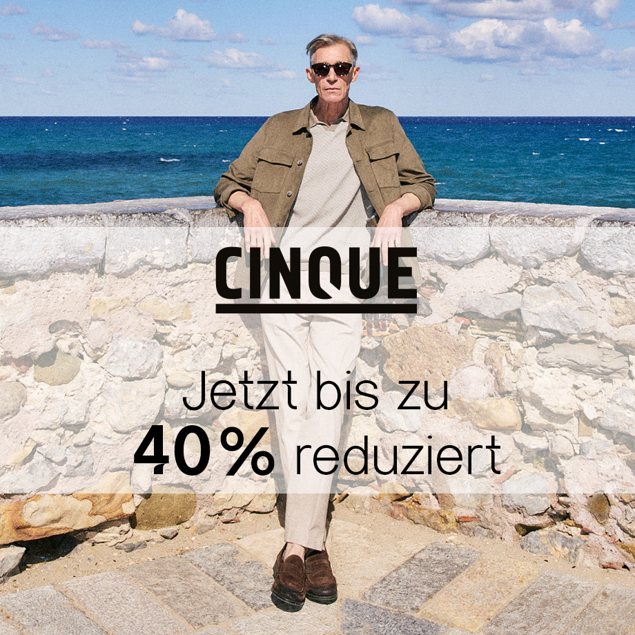 Mann in Beige-Hose und brauner Jacke vor Meer und Steinwand