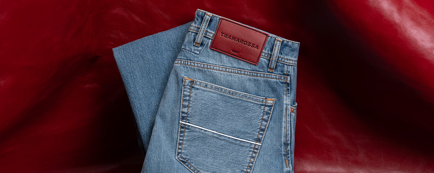 Hellblaue Jeans mit rotem Lederetikett, klassische Passform, auf rotem Hintergrund drapiert