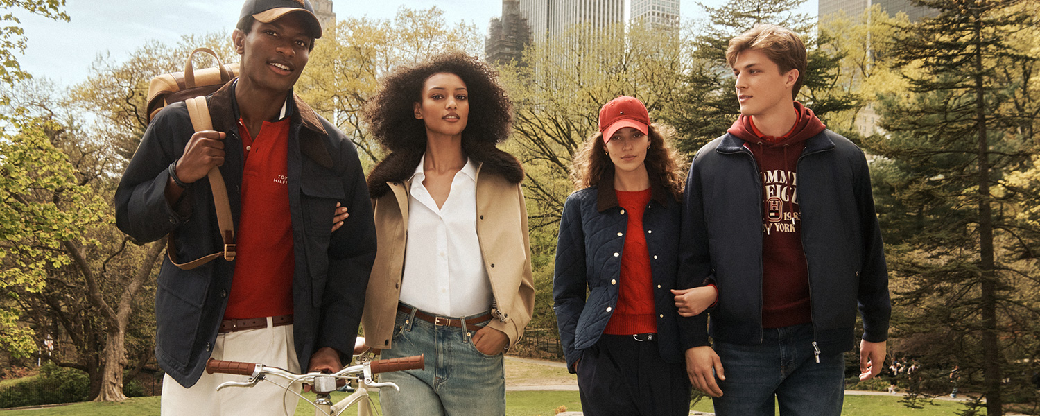 Gruppe in Freizeitkleidung: Männer in blauen Jacken, eine mit Kapuze, Frauen in beige Mantel und gestepptem Blouson, parkähnliche Umgebung.