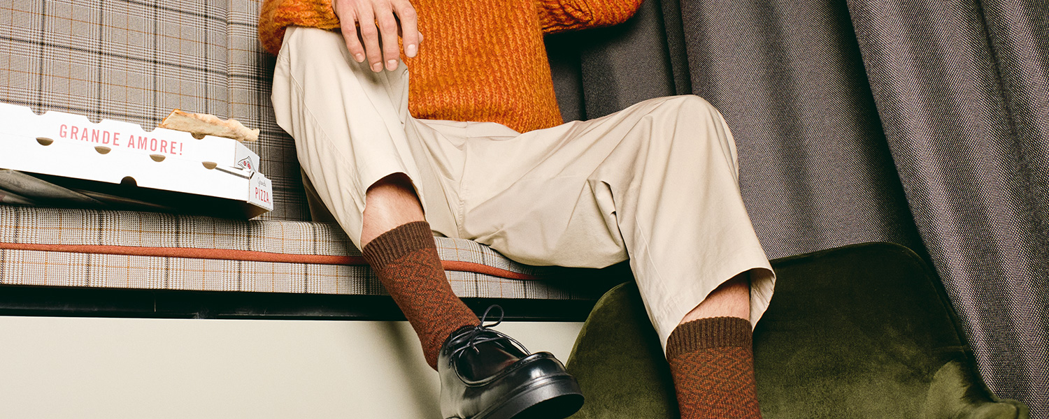 Hellbeige Chinohose, leger getragen mit orangefarbenem Strickpullover und schwarzen Lederschuhen