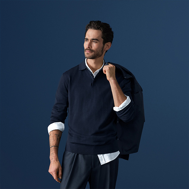 Mann in marineblauem Pullover über weißem Hemd, Blazer über der Schulter