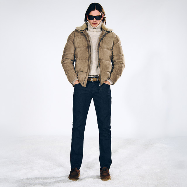 Hellbraune Daunenjacke und Rollkragenpullover aus Wolle, dunkelblaue Jeans, Mann stehend vor weißem Hintergrund