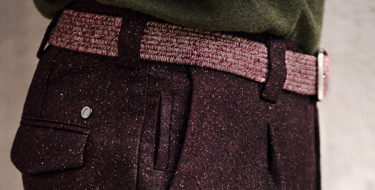 Elegante Anzughose mit weinrotem Tweed-Muster und geflochtenem Gürtel, getragen mit grünem Pullover