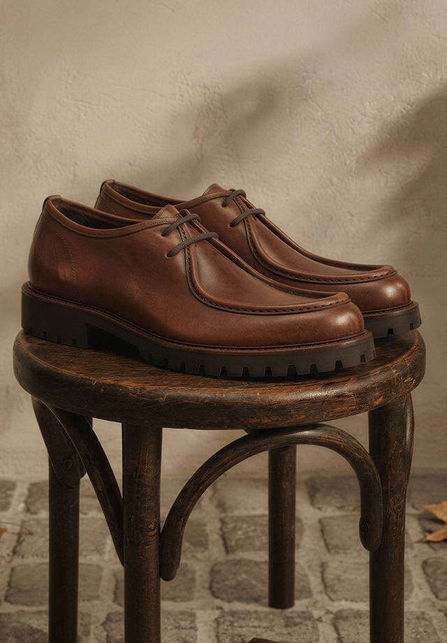 Braune Lederschuhe mit Profilsohle auf Holzstuhl präsentiert, elegantes Design